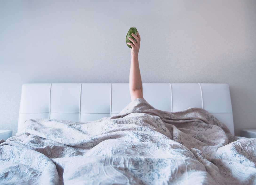 Woman in bed with avocado in raised hand