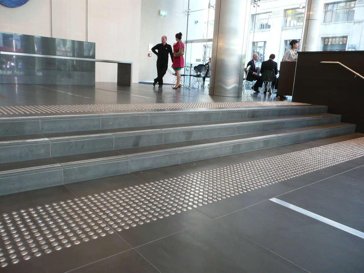 Stainless steel tactile indicators on tiles at top and bottom of stairs
