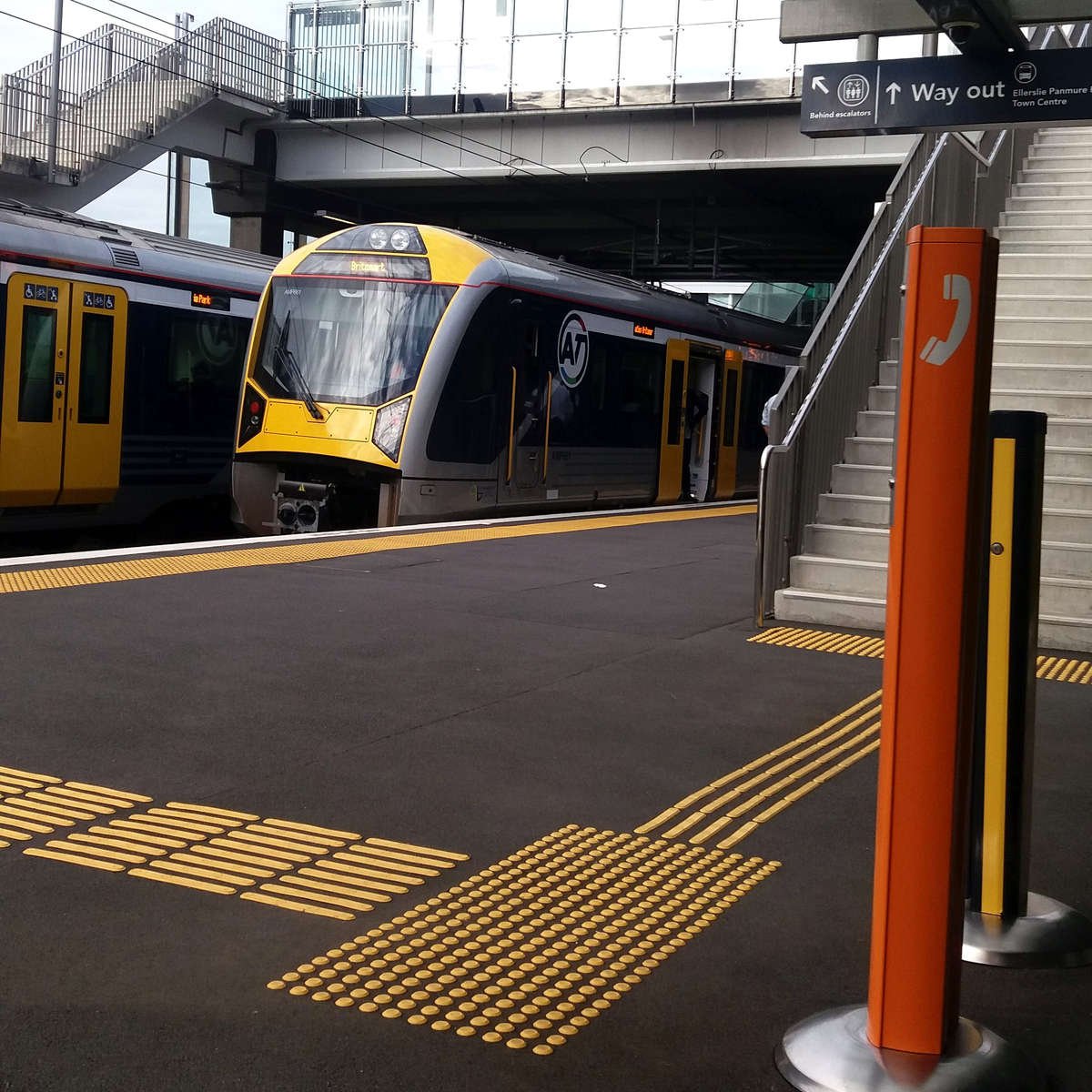 TacPro yellow polyurethane warning and directional tactile indicators installed on platform edge and misc help points/fare payment devices. Two trains pass each other.
