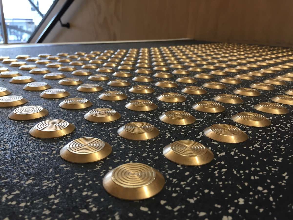 TacPro brass tactile indicators installed on black lino with white speckles at top of stairs
