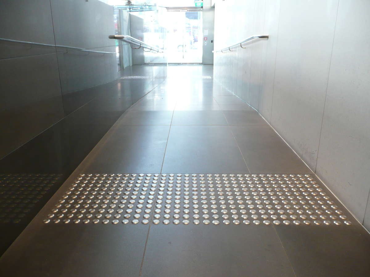 Stainless steel tactile indicators on tiles at top of ramp