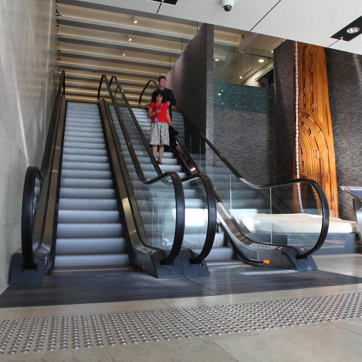 People descend escalators with TacPro stainless steel tactile indicators installed to top and bottom