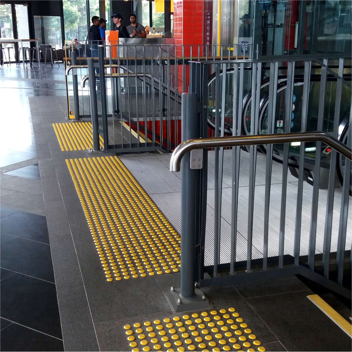 TacPro polyurethane tactile indicators installed to grey tiles at top of stairs and escalators