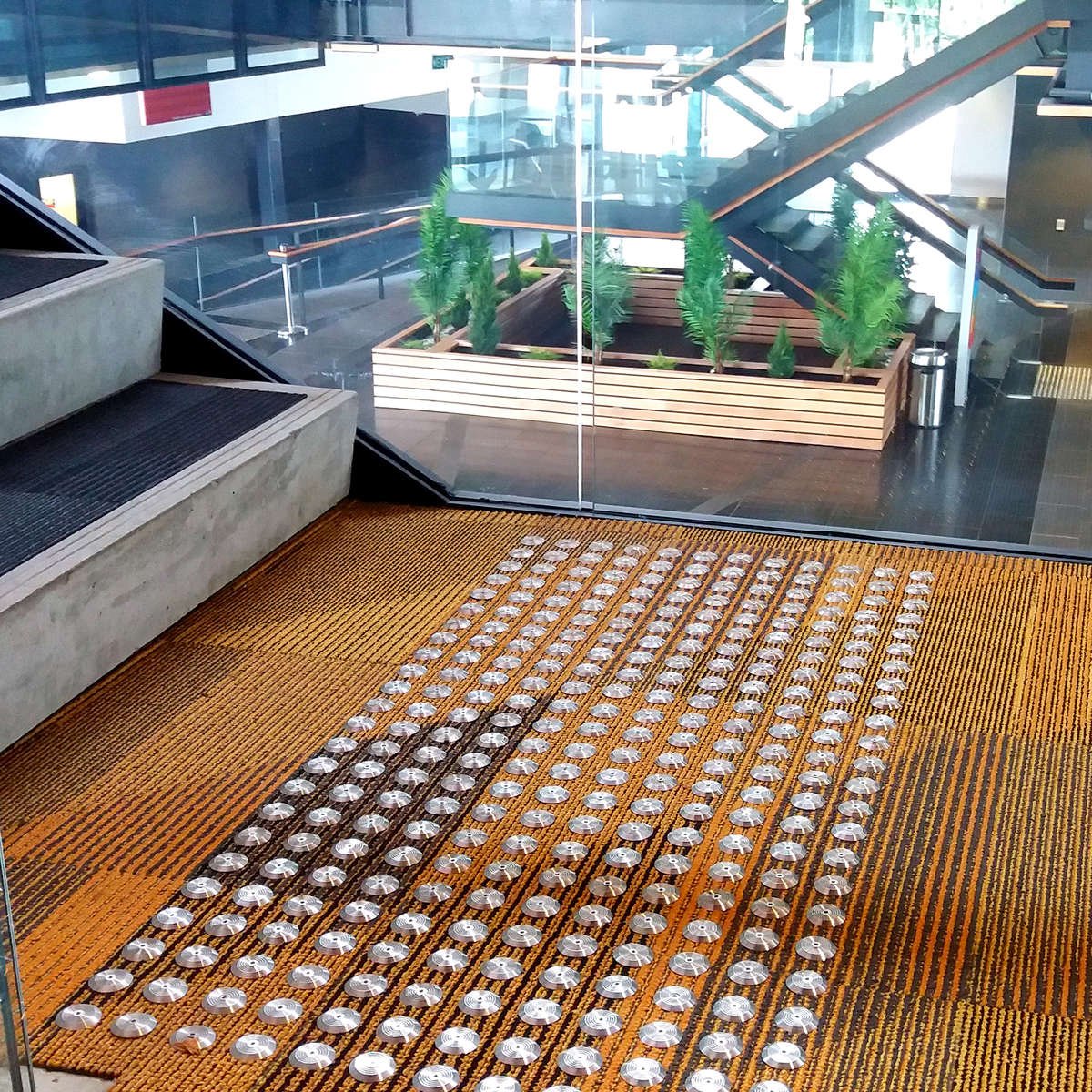 TacPro stainless steel tactile indicators installed to orange/black carpet at bottom of stairs
