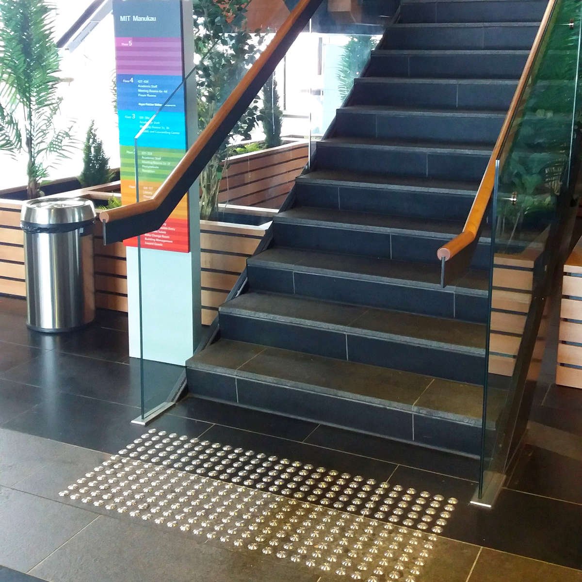 TacPro stainless steel tactile indicators installed to dark tiles at bottom of stairs