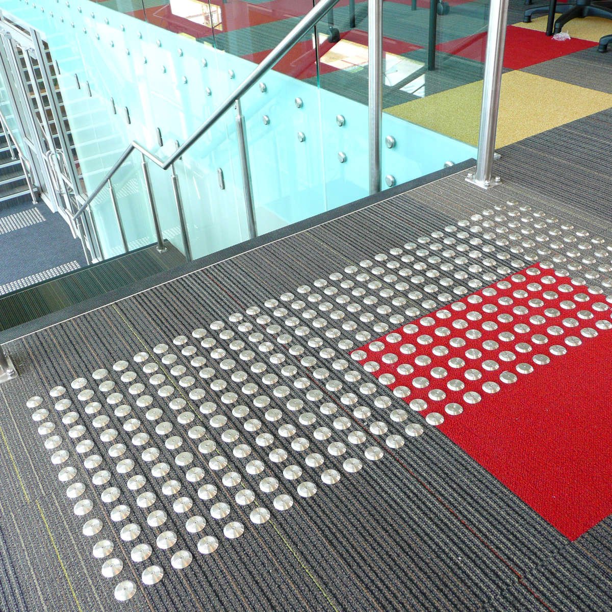 TacPro stainless steel tactile indicators on grey/red carpet at top of stairs