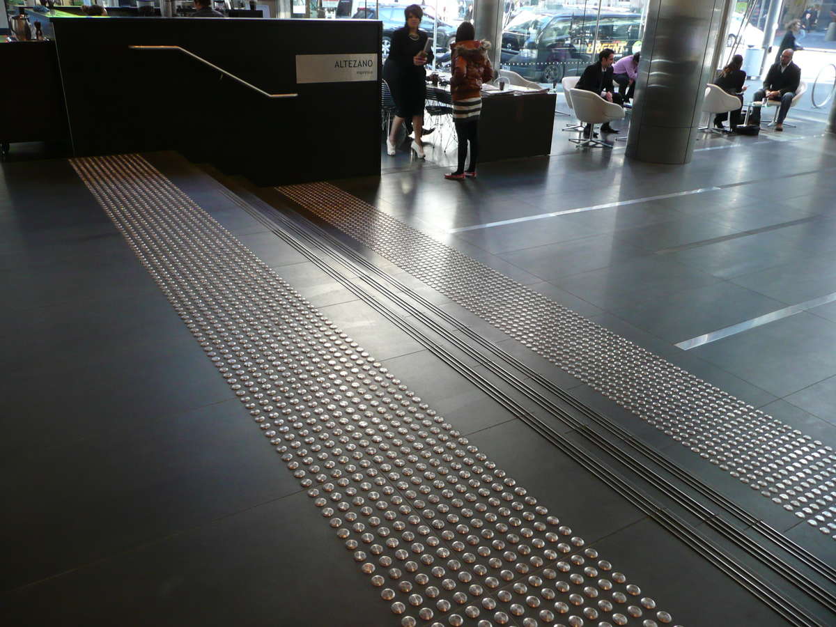 Stainless steel tactile indicators on tiles at top and bottom of stairs