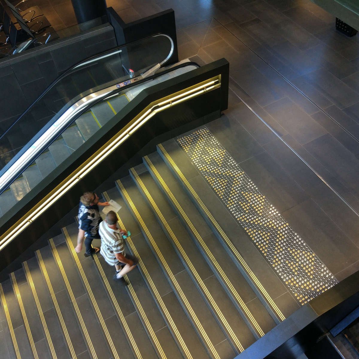 Distance photo with people walking on TacPro brass, stainless steel, and stainless steel with black carborundum arranged in a pattern at the top of stairs