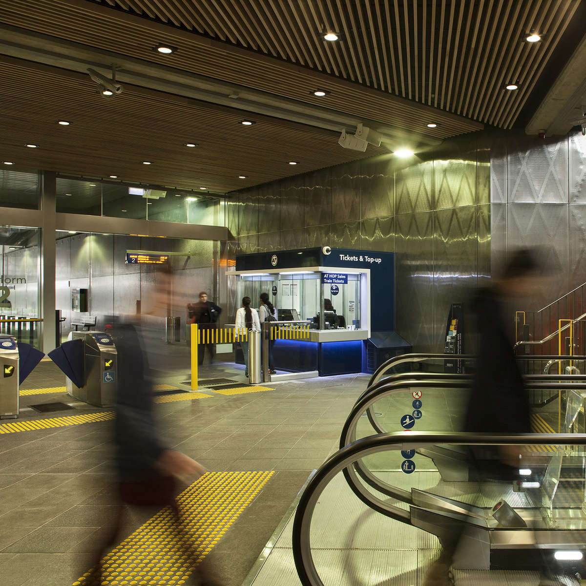 View of ticket booth with TacPro yellow polyurethane tactile indicators installed at ticket gates and bottom of escalator