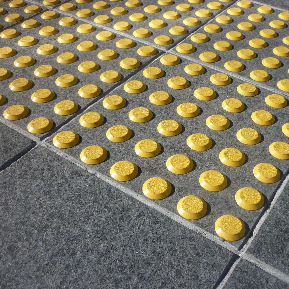 A close-up of TacPro yellow polyurethane tactile indicators installed on bluestone tiles at a courtesy pedestrian crossing.