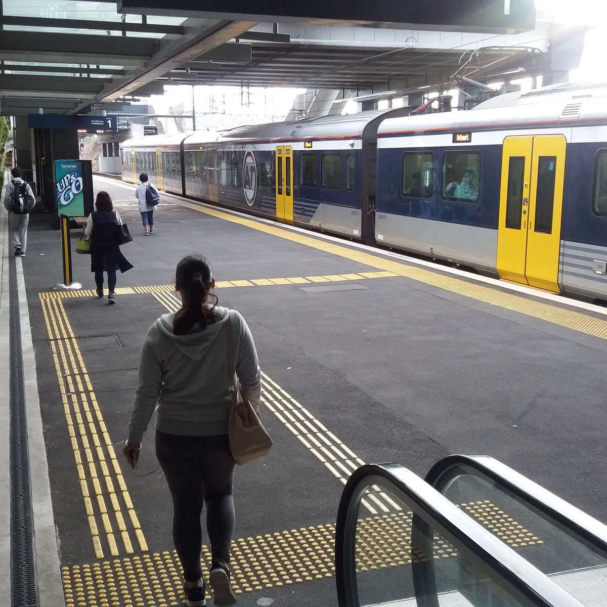 TacPro yellow polyurethane warning and directional tactile indicators installed on platform edge and misc help points/fare payment devices. Train sits at station.