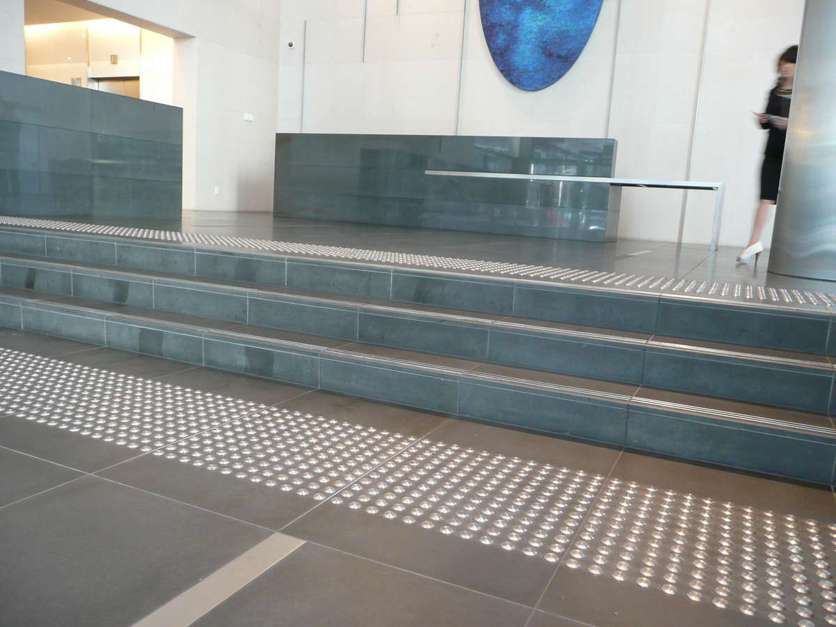 Stainless steel tactile indicators on tiles at top and bottom of stairs