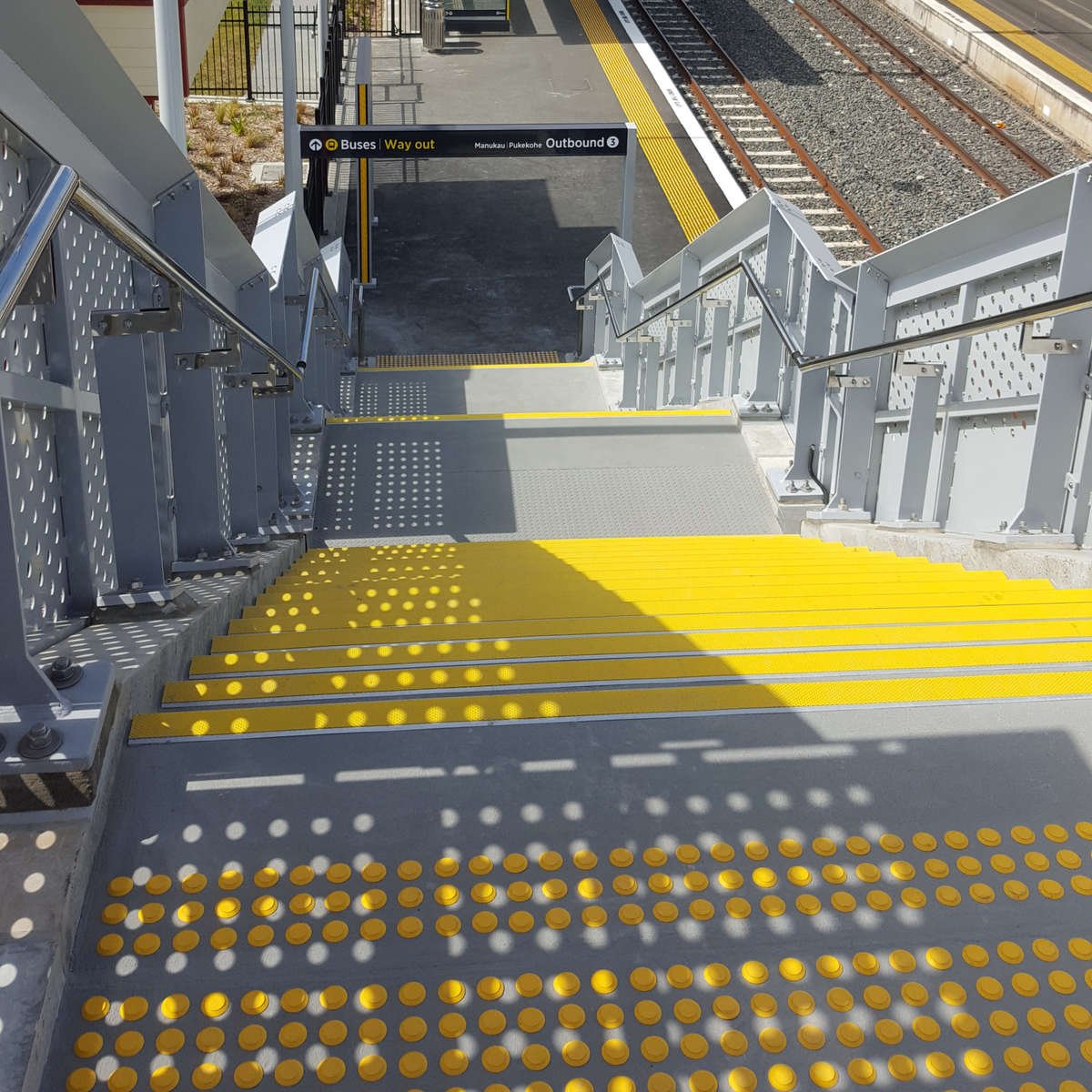 Yellow polyurethane tactile indicators and stair nosing on concrete at train station stairs
