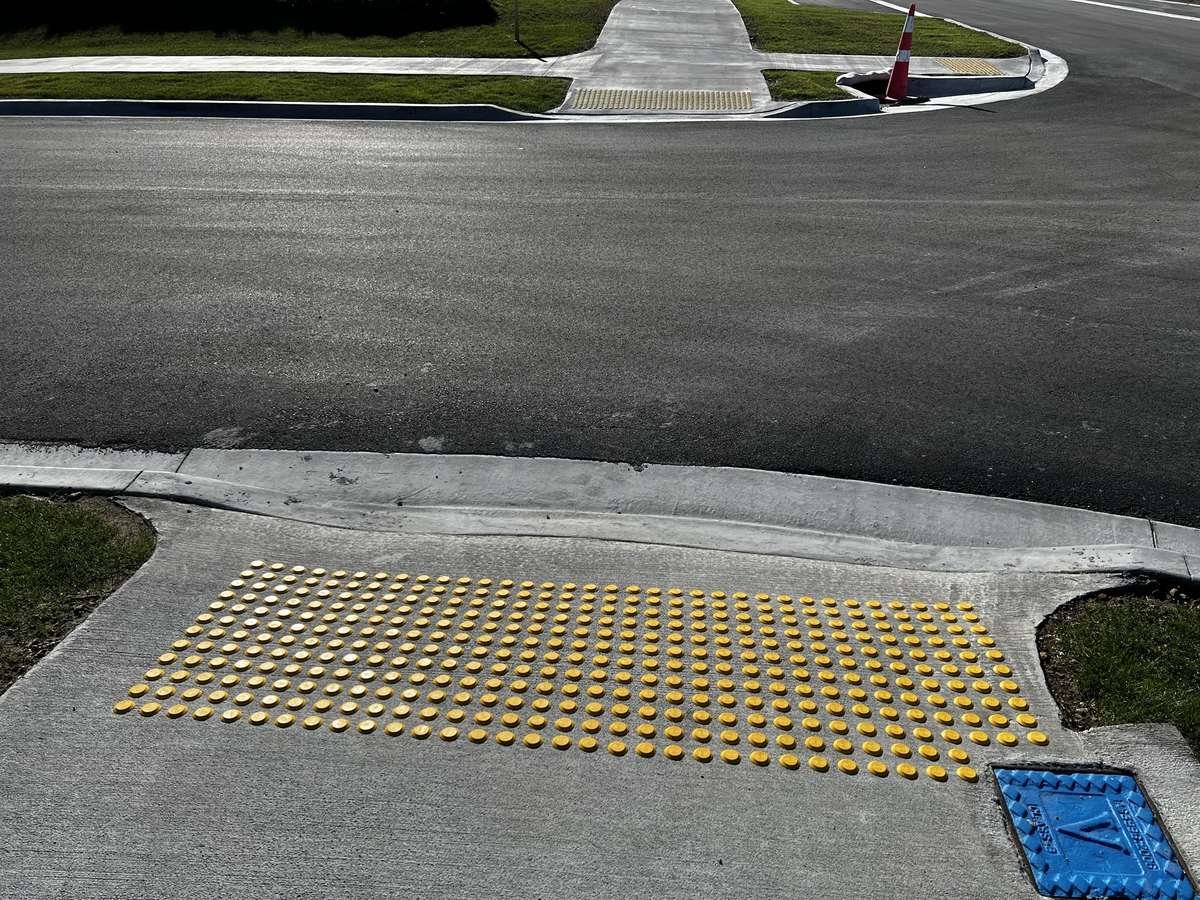 Yellow polyurethane tactile indicators on concrete at suburban pedestrian crossing/pram ramp