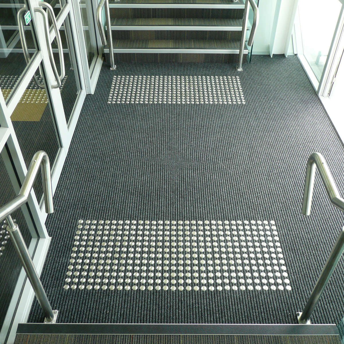 TacPro stainless steel tactile indicators on carpet in an entry foyer at the bottom of stairs