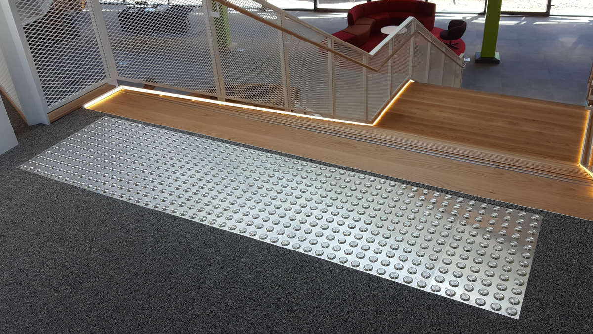 TacPro stainless steel tactile indicator plates installed to carpet at top of timber stairs