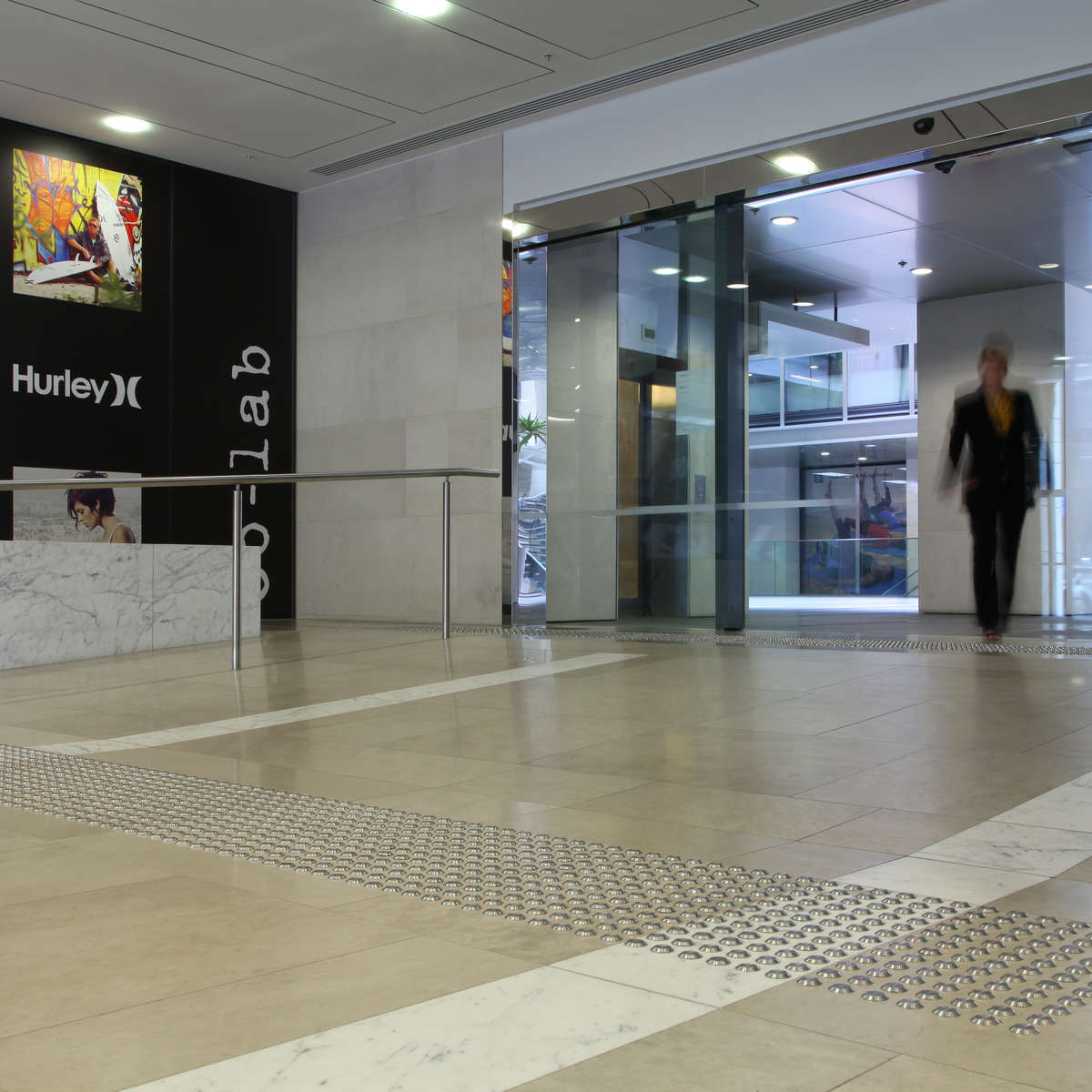 Lady approaches from door way and prepares to descend ramp with TacPro stainless steel tactile indicators installed at the top and bottom