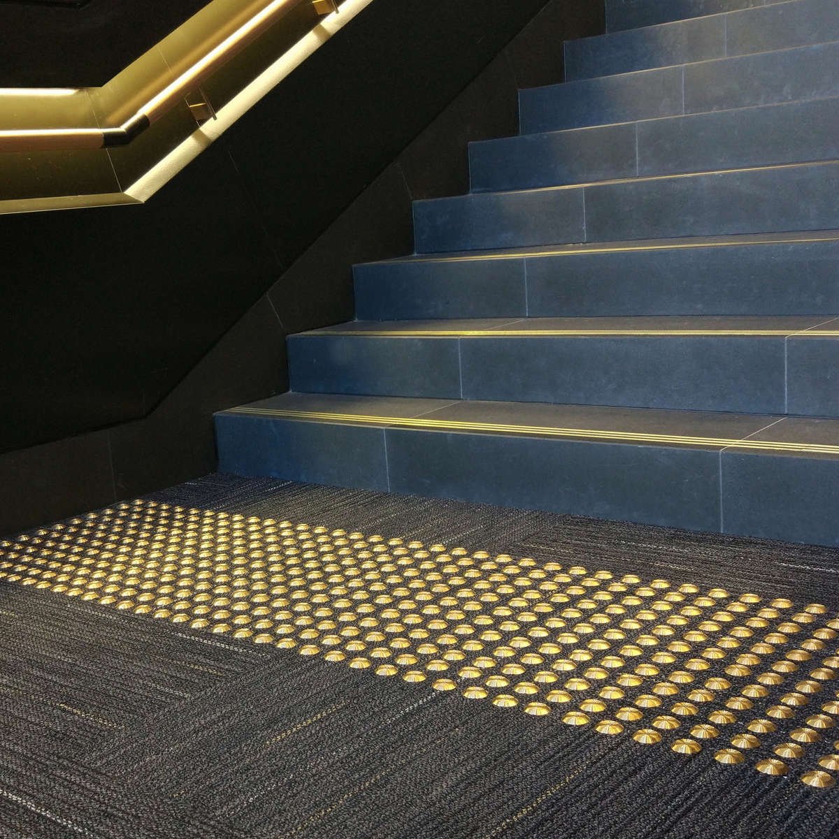TacPro Brass tactile indicators on dark carpet at bottom of stairs