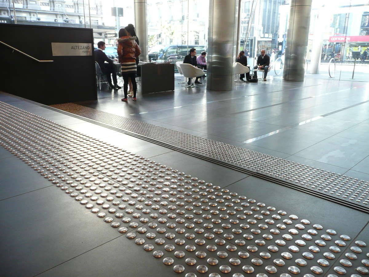 Stainless steel tactile indicators on tiles at top and bottom of stairs