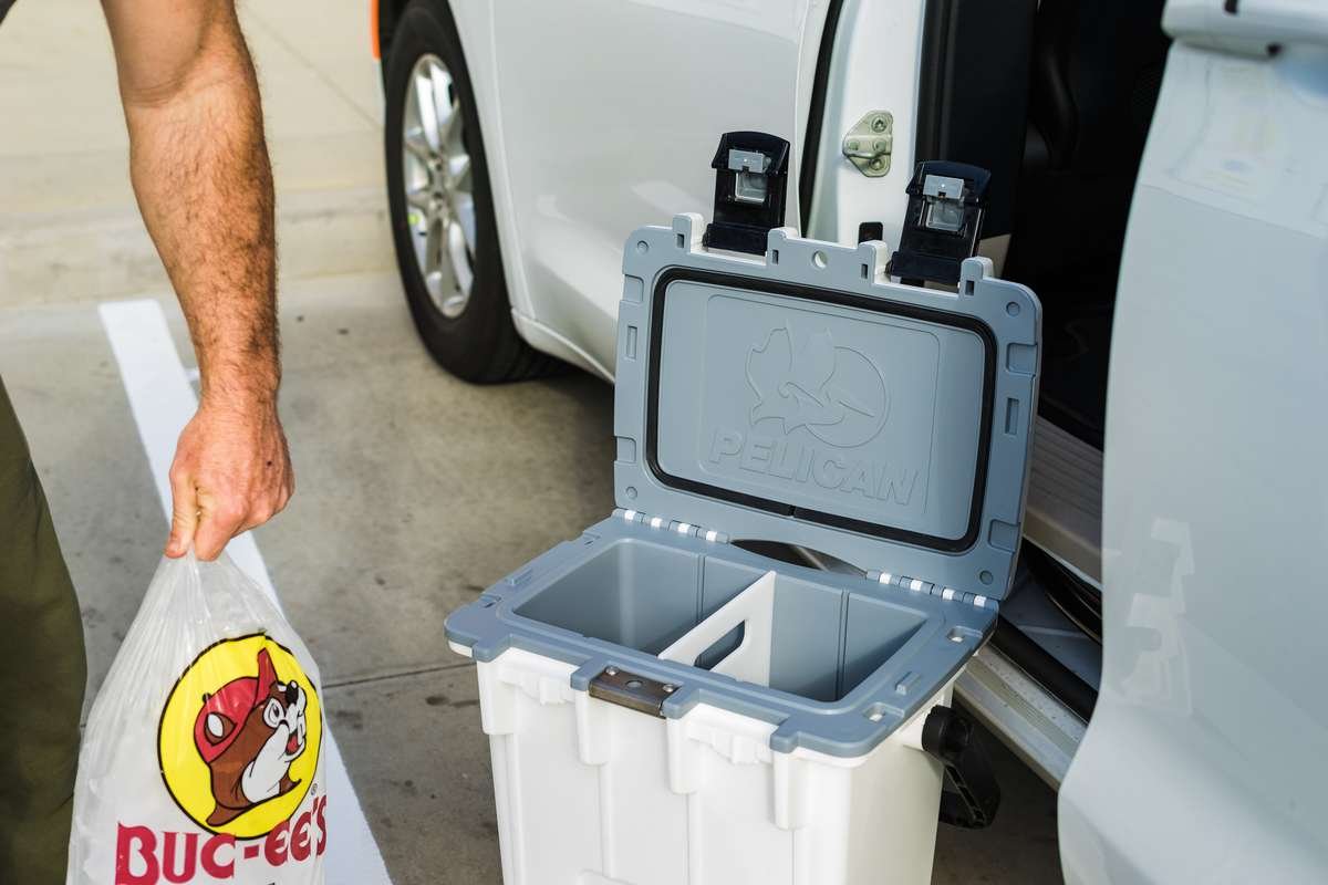 A person holding a bag of cubed ice while standing next to an open Pelican Elite Cooler.