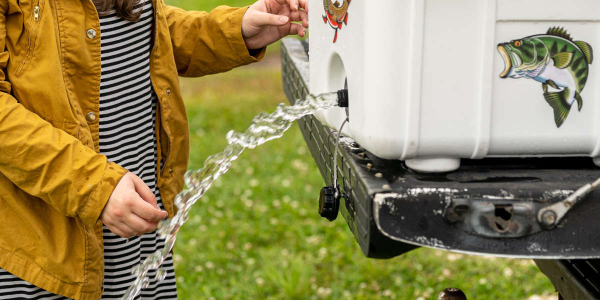 A stream of water pours out of the drain of a Pelican Elite Cooler as a person watches.