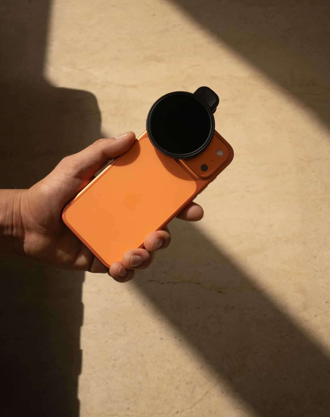 Person holding orang iPhone with hybrid filter attached.