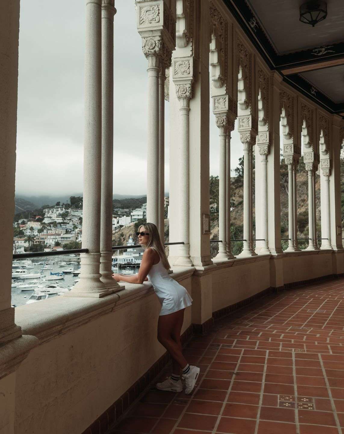 Woman leaning on a balcony with ornate columns overlooking Catalina Island’s harbor, captured on iPhone using SANDMARC gear — showcasing depth, symmetry, and leading lines in iPhone photography.