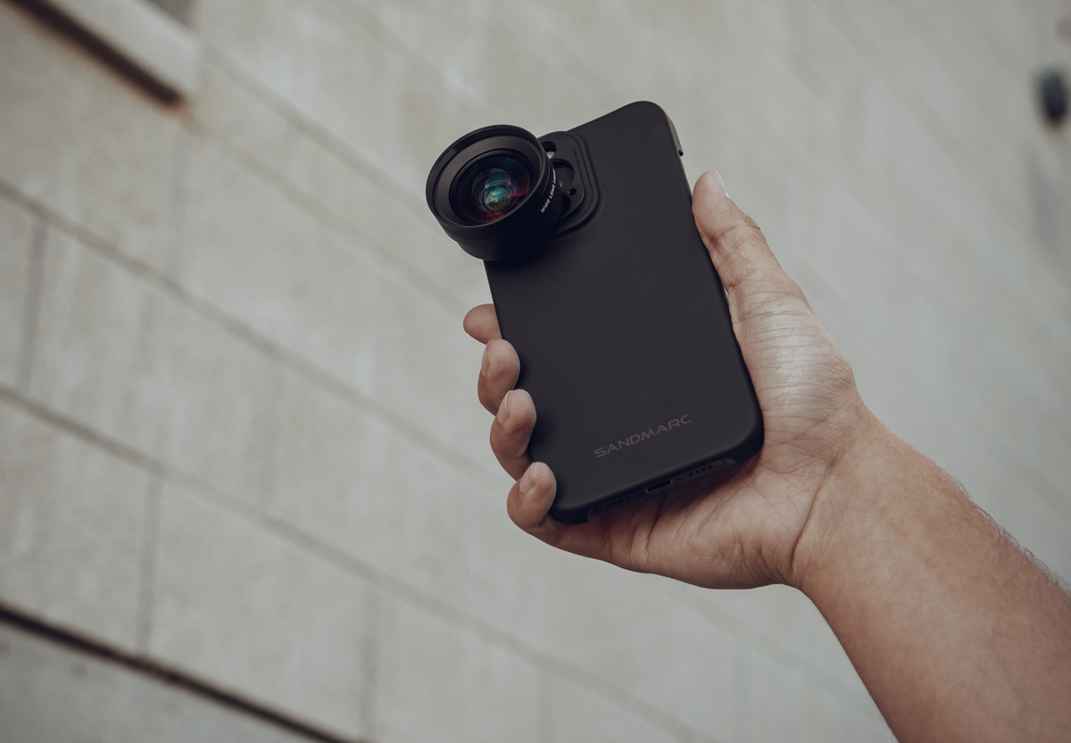 Wide Lens attached to black iPhone case in front of cement wall.