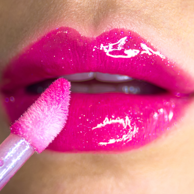 Lip gloss being put on pink glittery lips.