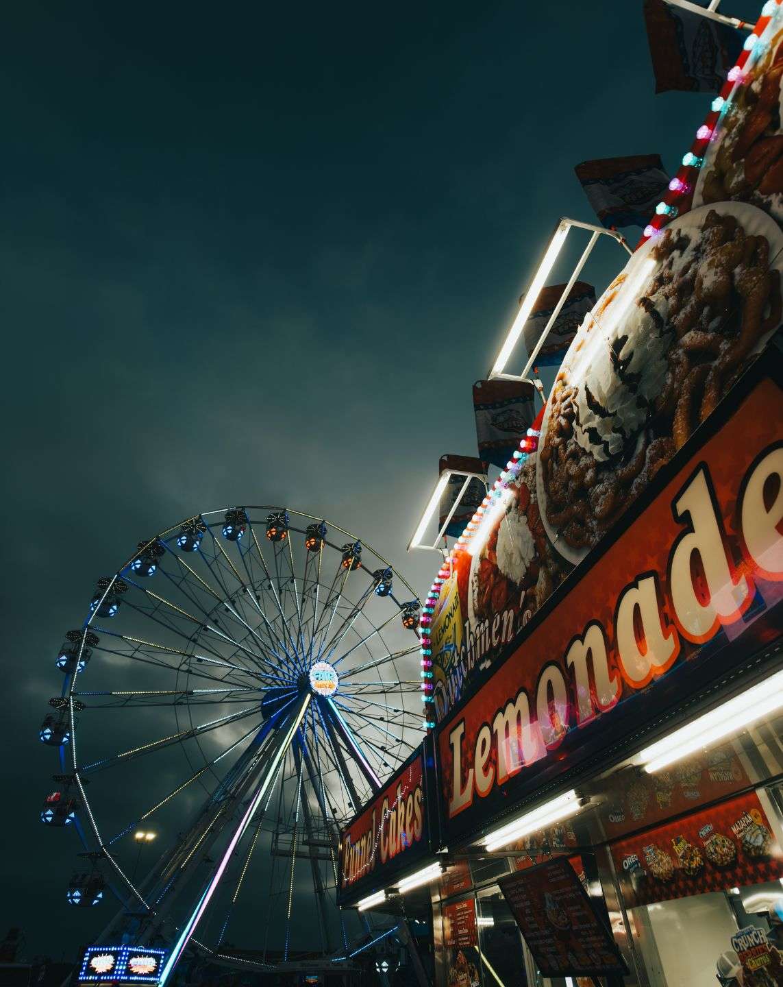 Nighttime carnival scene captured on iPhone using SANDMARC gear — a glowing Ferris wheel and colorful lemonade stand illuminated under moody skies, showcasing vibrant lighting and contrast in iPhone photography.