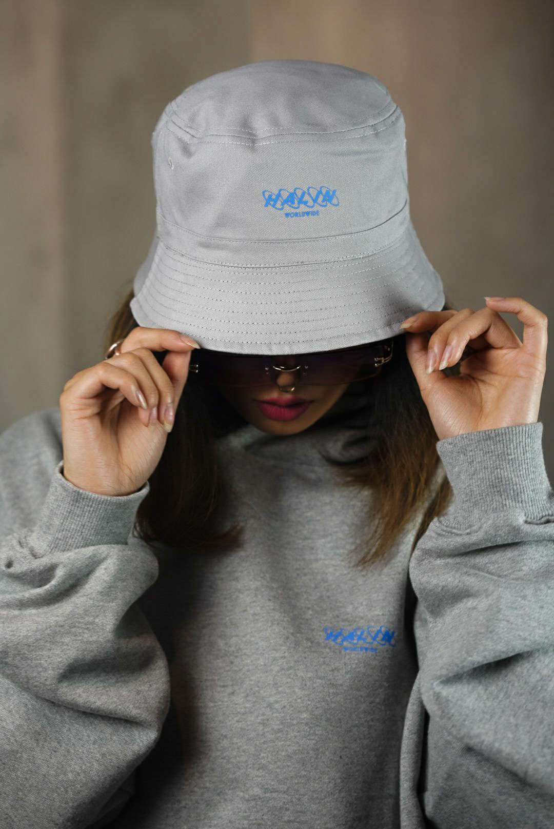 Female streetwear model wearing reversible bucket hat and grey oversize hoodie from Halin. Female streetwear model wearing reversible bucket hat and grey oversize hoodie from Halin.