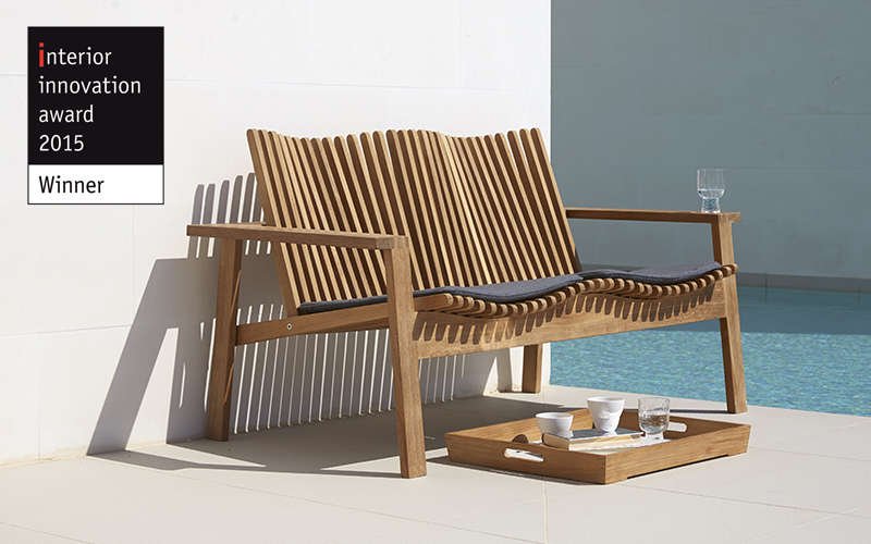 Teak bench with dark grey cushions with a teak servering tray with coffee cups and water glass by the pool