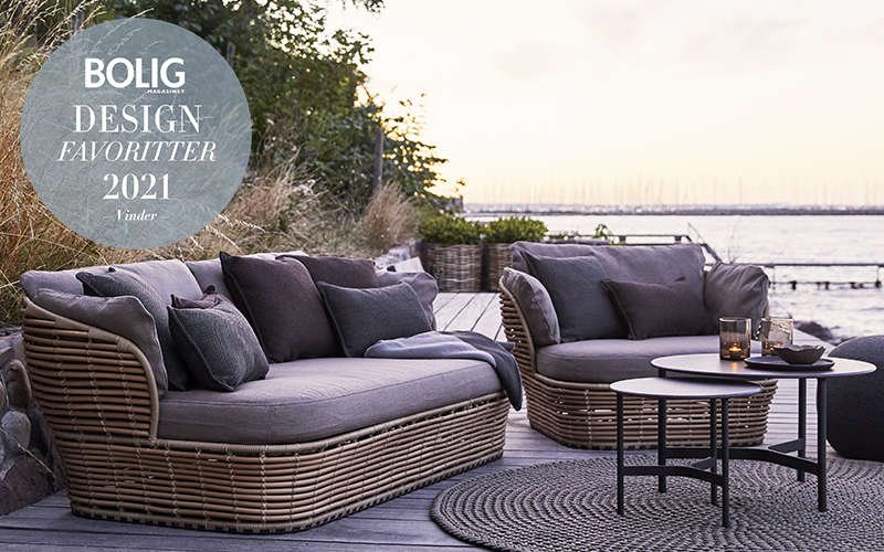 Outdoor lounge furniture of natural material with grey cushions and round side tables