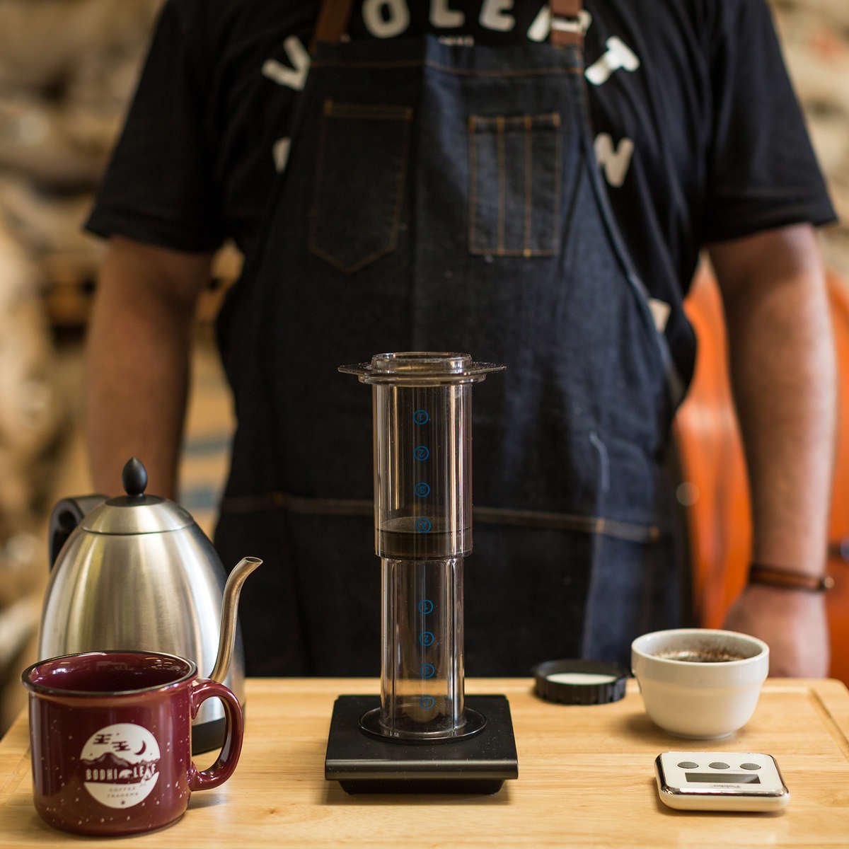 Barista with Aeropress on scale, with mug and kettle.