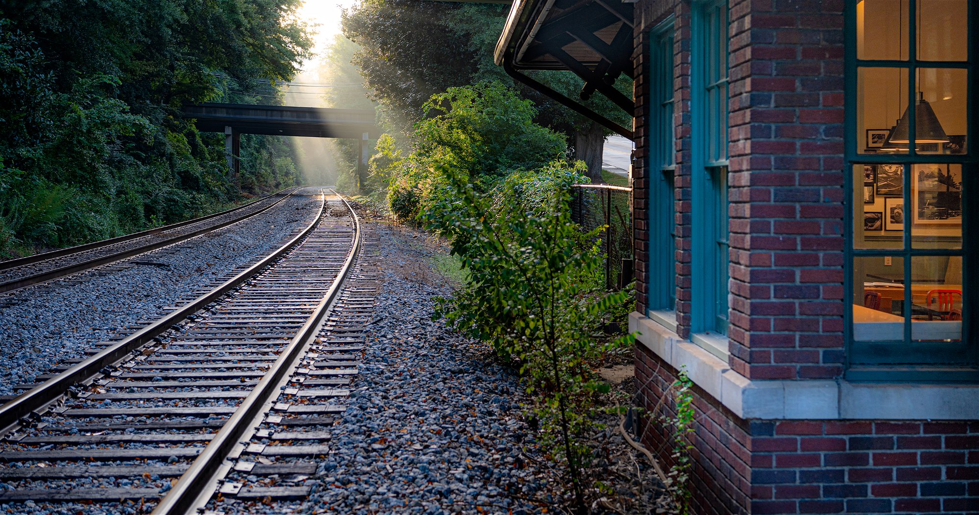 Sun rays break through mist at dawn, as Kaldi's Depot cafe sits beside train tracks.