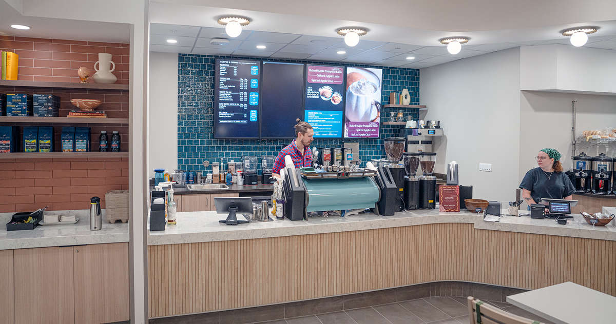 A wide view of the SCC cafe, showing retail and a condiment bar on the left, then the espresso bar, then the register and pastries on the right