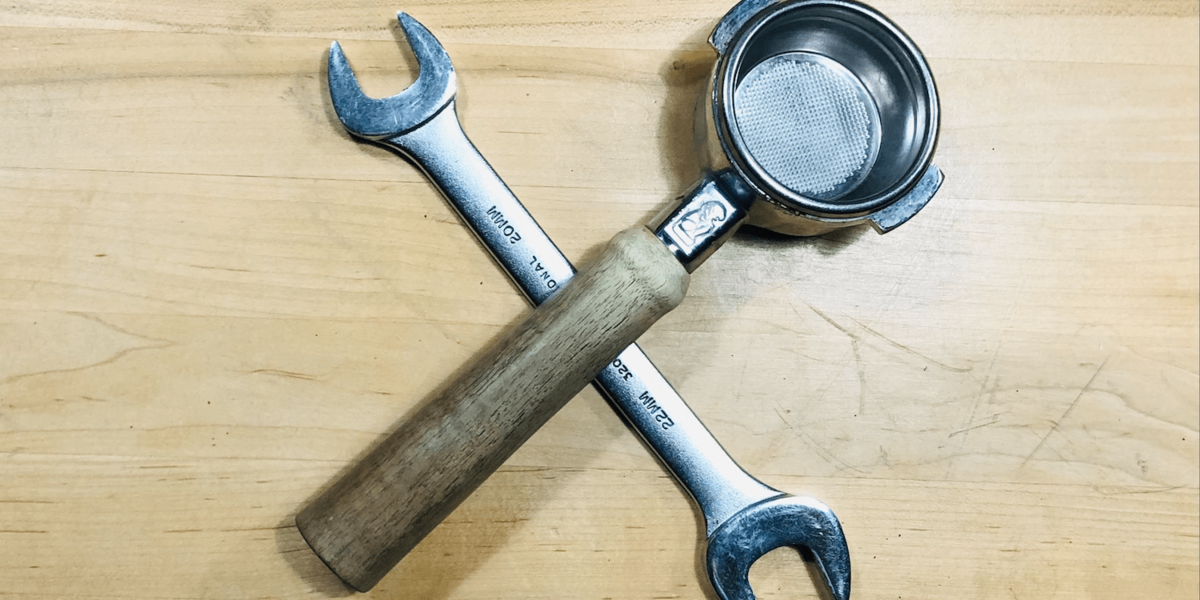 A wrench and an espresso portafilter on a wooden table