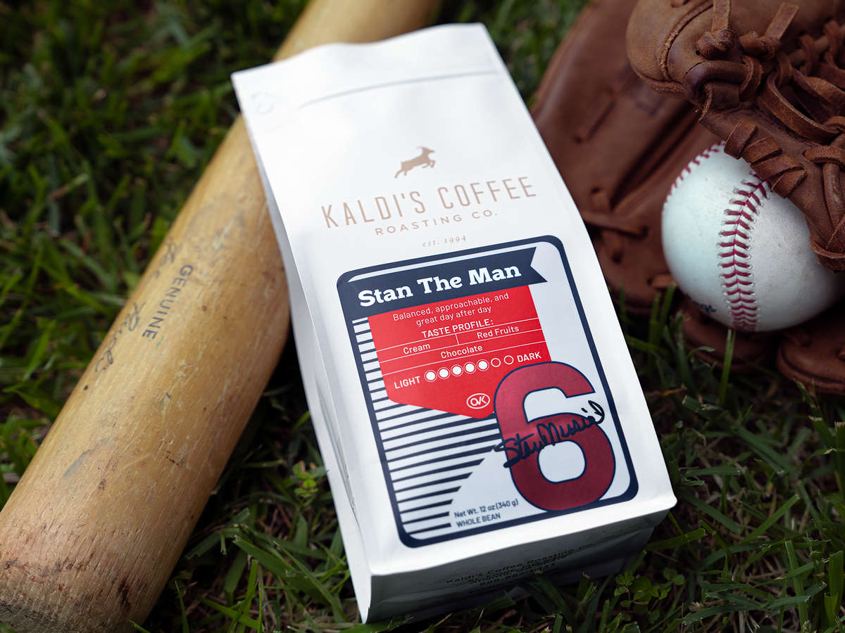 A bag of Stan the Man Blend rests against a baseball bat and glove on grass. The glove holds a baseball