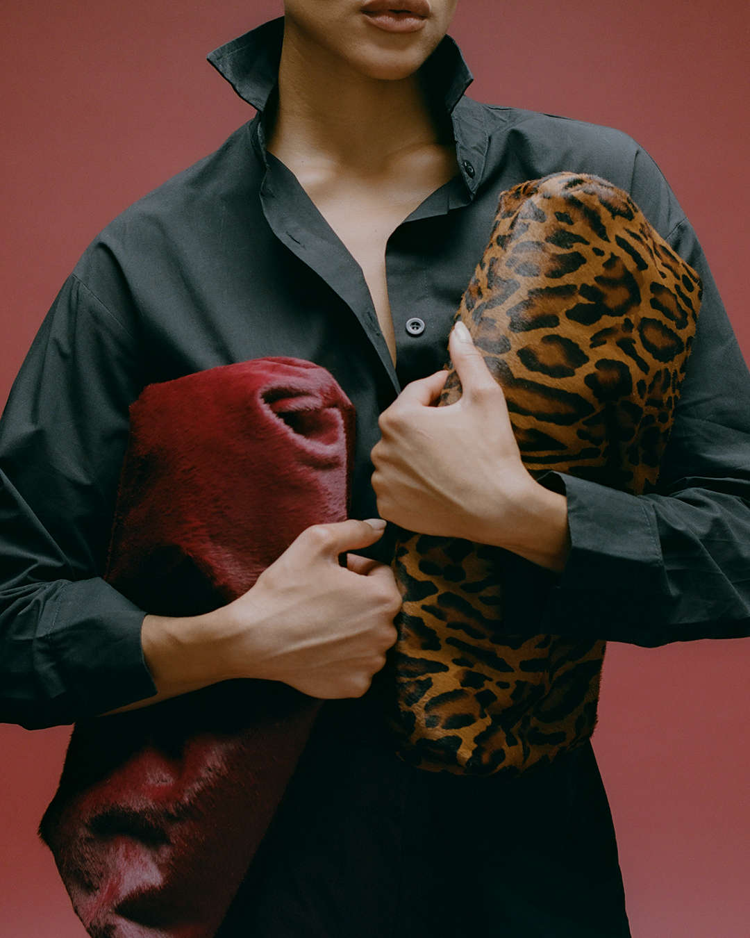 model holding a leopard print and a burgundy calf-hair textured clutch
