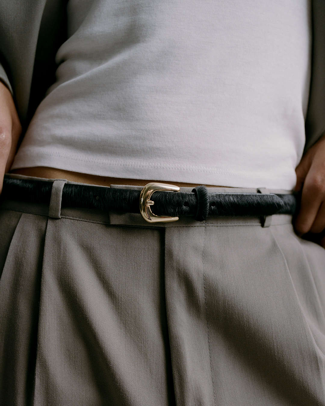 close up of a skinny black calf-hair belt with a gold buckle on a grey suit