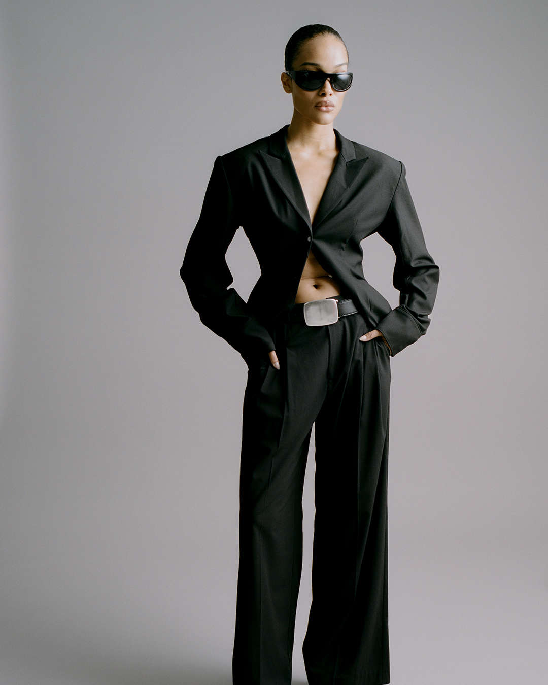 model wearing a black suit and black sunglasses with a black leather belt that has an oversized silver plaque buckle