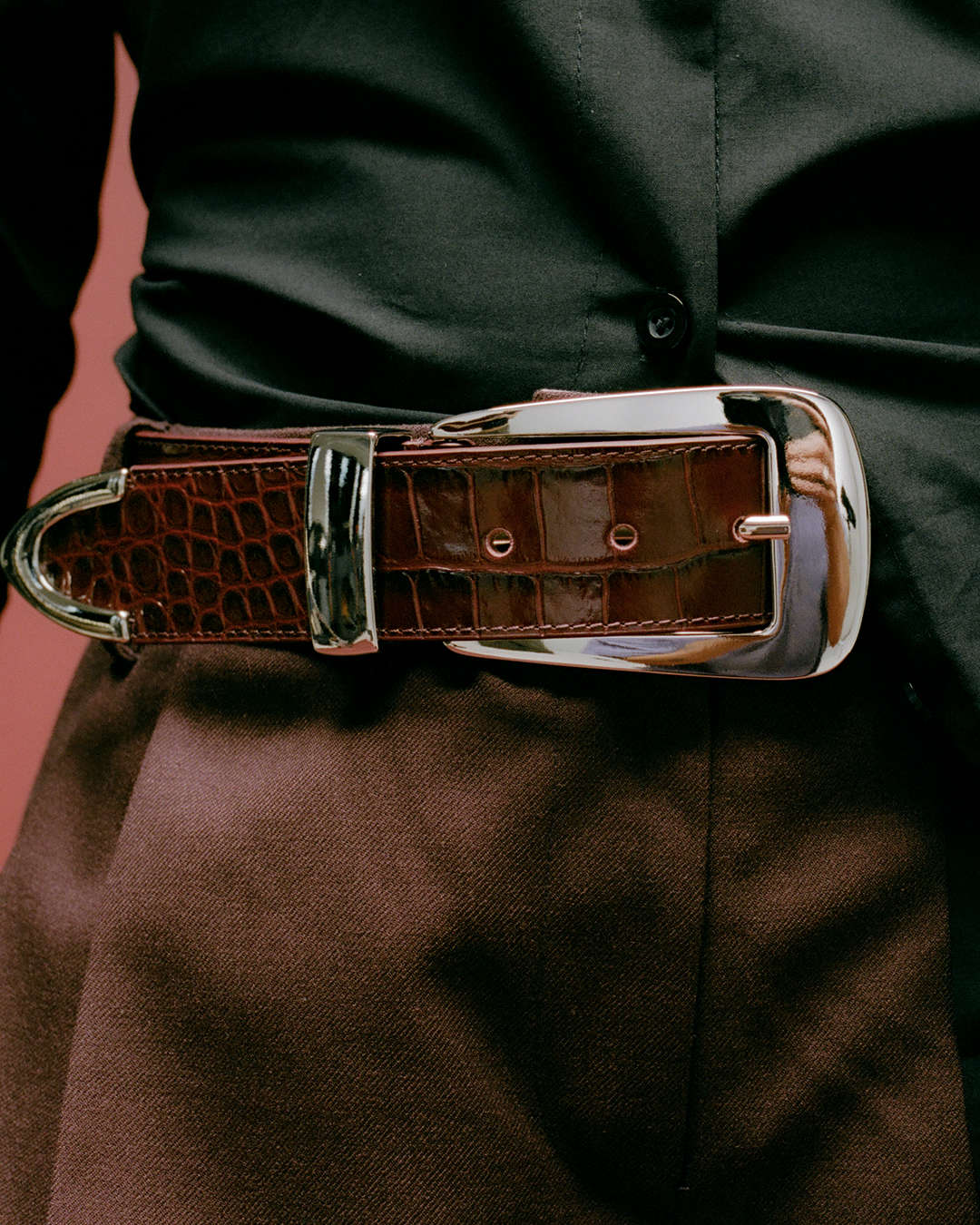 close up of a croc-printed burgundy belt with oversized buckle in silver
