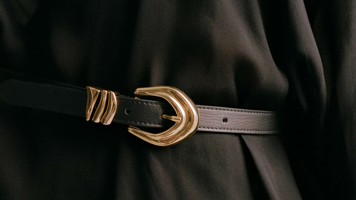 a black skinny leather belt with detailed gold hardware close up on a black top