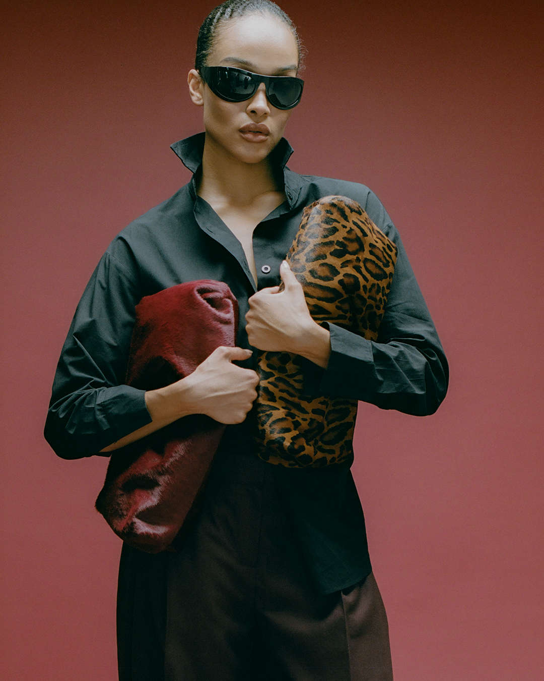 model holding a leopard print and a burgundy calf-hair textured clutch