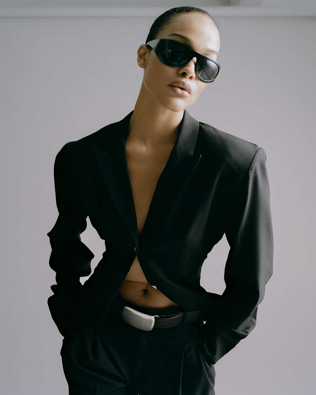 model wearing a black suit and black sunglasses with a black leather belt that has an oversized silver plaque buckle