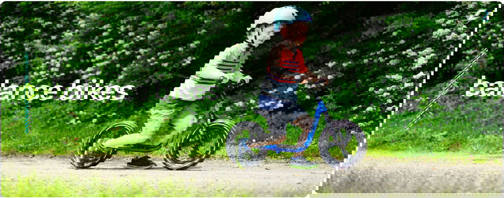Balance Bikes - Excited toddler with Bright Blue Multi-Sport Helmet and Blue Kazam Pro with Magwheels - Riding along a dirt path with beautiful green nature and white flowers along the background Balance Bikes - Excited toddler with Bright Blue Multi-Sport Helmet and Blue Kazam Pro with Magwheels - Riding along a dirt path with beautiful green nature and white flowers along the background