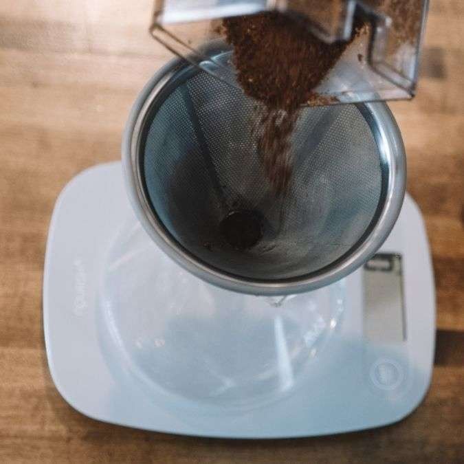 Coffee grinds being poured into the dripper on a scale