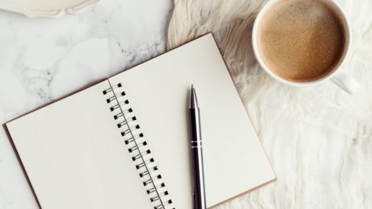 Notebook opened to clean page with pen and coffee